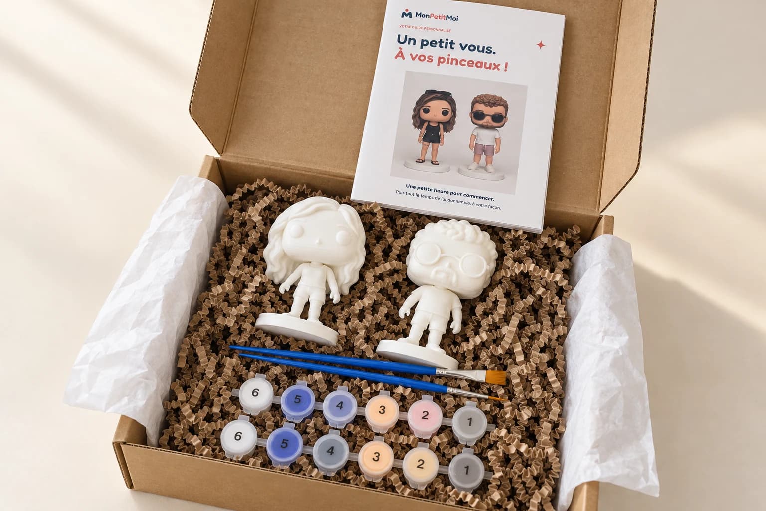 Kit MonPetitMoi ouvert avec figurines à peindre, pinceaux et peintures. Photo retouchée.